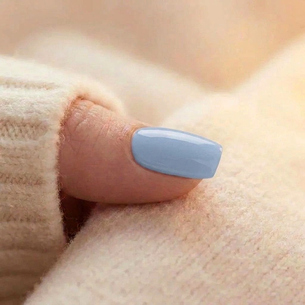 Närbild på en Baby Blue press-on nagel i mjuk ljusblå, fyrkantig form med blank gelé-finish på tumme