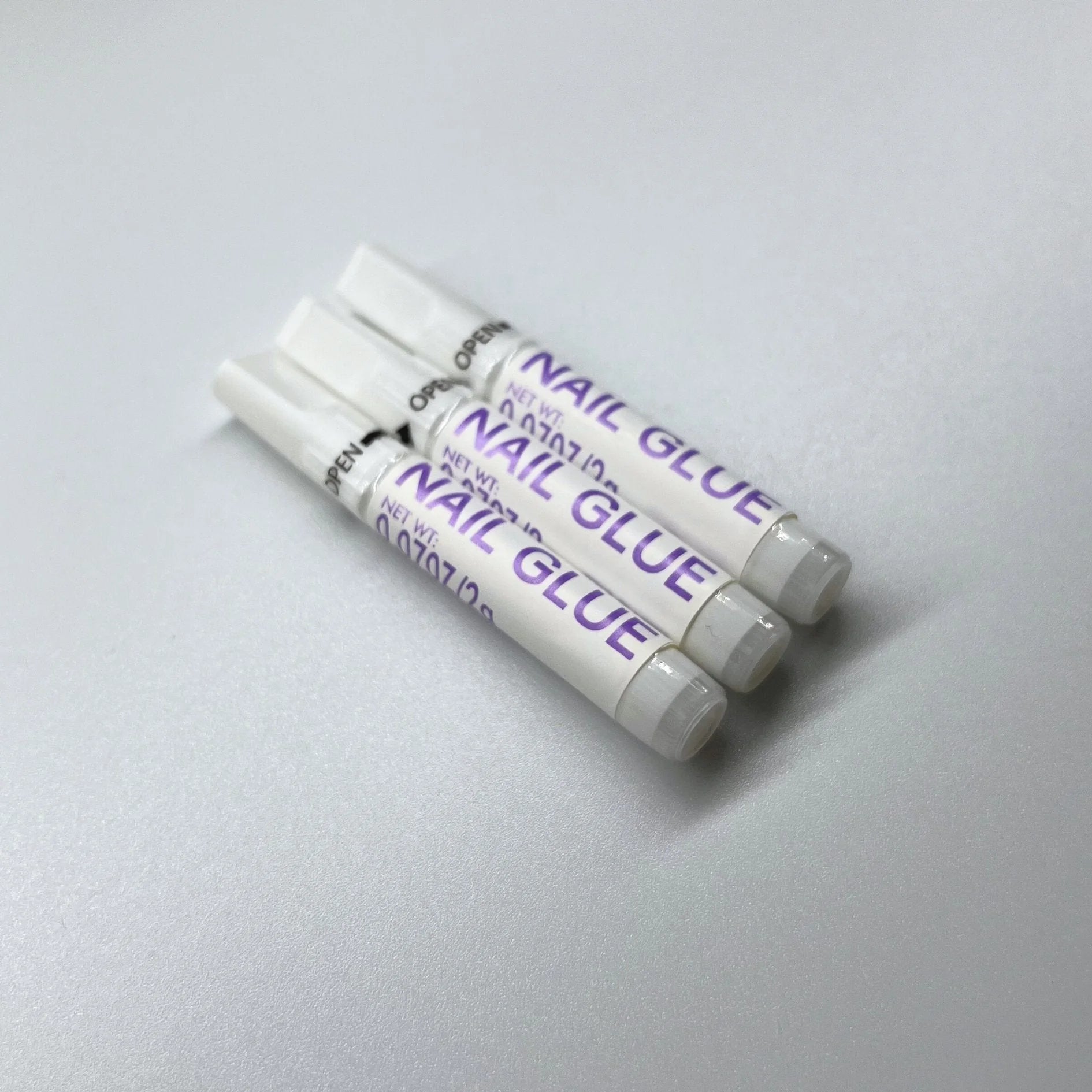 XGlue nagellim närbild – tre tuber Nail Glue med open-pil och applikatorspets