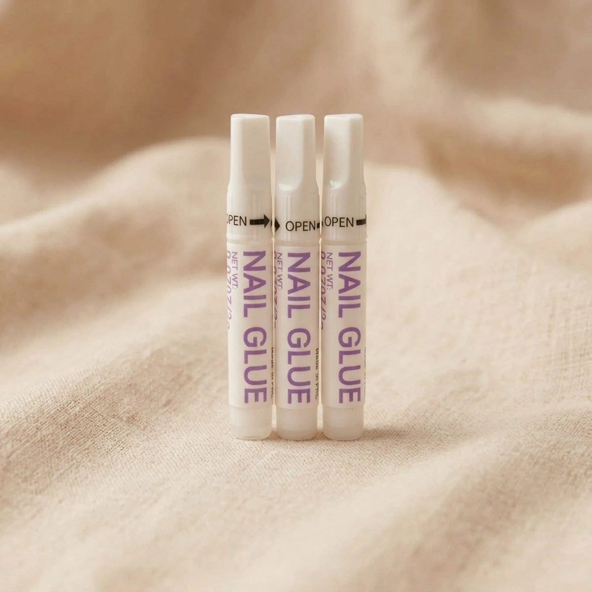 XNails Nail Glue nagellim på beige bakgrund