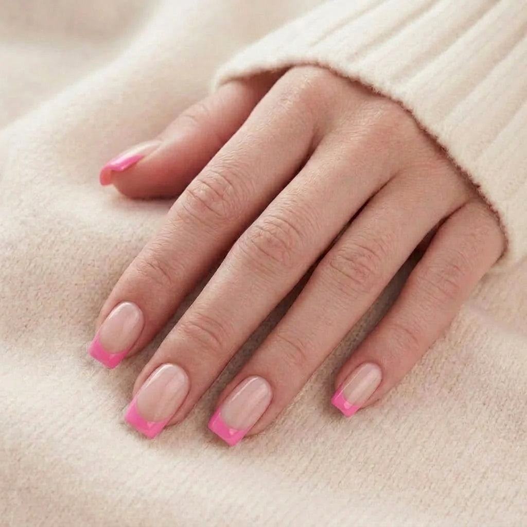 Pixie Pink press-on naglar i kort square med nude bas och klar rosa French-tip på hand mot beige stickad tröja
