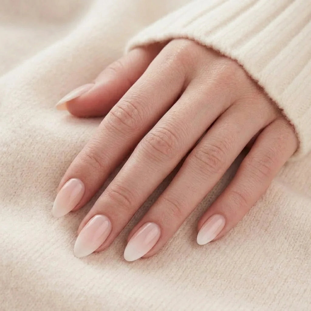 Mandelformade naglar i rosa och vit fransk ombré på hand mot ljus stickad tröja