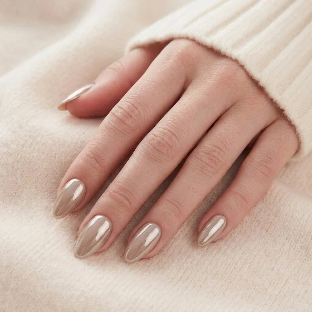Elegant hand med mandelformade taupe press-on naglar med metallic glans mot en mysig krämvit tröja