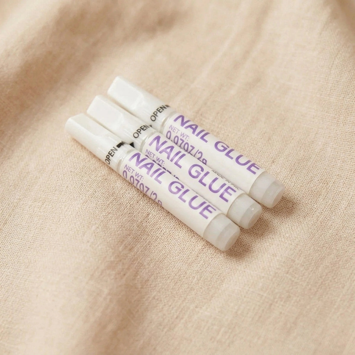 XNails Nail Glue nagellim på beige bakgrund