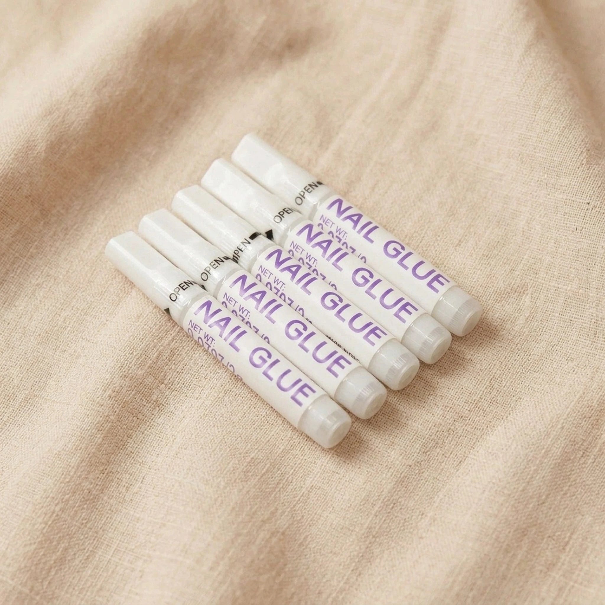 XNails Nail Glue nagellim på beige bakgrund