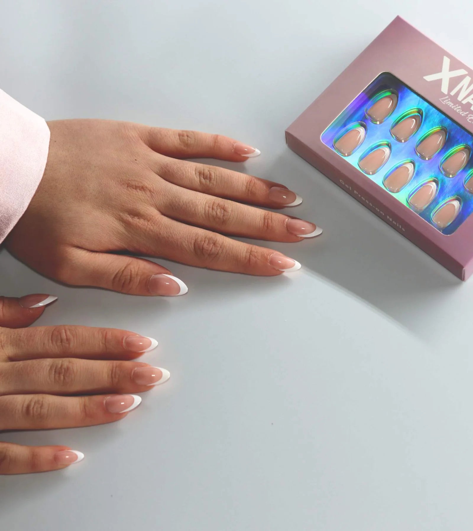 Två händer med franska press-on-naglar bredvid den rosa XNails-asken